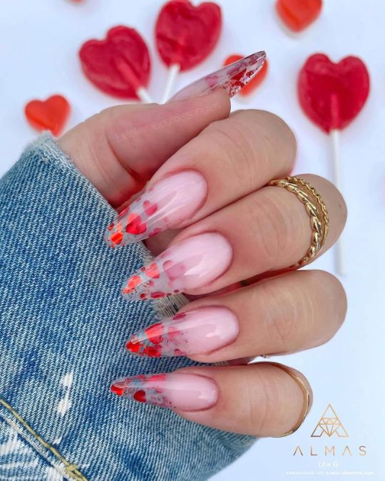 long stiletto nails showcase a delicate pink base, dramatically accented with bold red petal-like designs at the tips