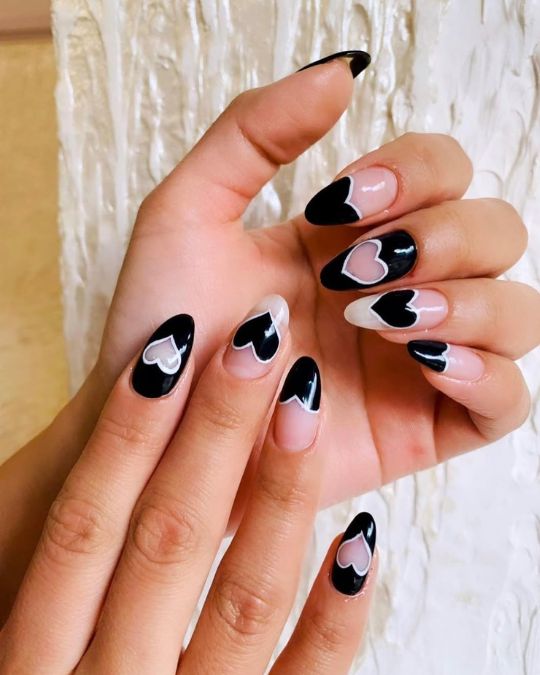 Almond-shaped nails feature a sophisticated black and nude color scheme, artfully decorated with playful heart cutouts