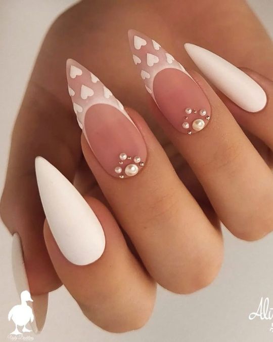 stiletto nails showcase a gentle blend of soft pink and white, adorned with intricate heart patterns and lustrous pearl embellishments