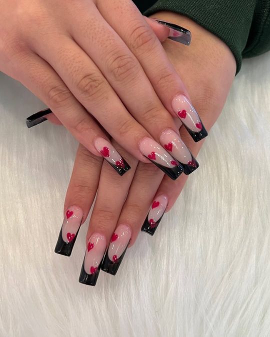 Long square nails with a nude base, black French tips, and scattered red heart accents for Valentine's Day Nail